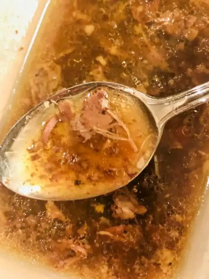 Beef barbacoa broth called consomé. There is a spoon containing some of the consomé in the foreground.