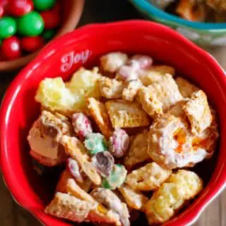 A red bowl containing Christmas White Chocolate Cheddar Texas Trash with a bowl containing green and red M&M's in the background.