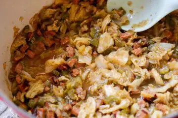A red Dutch oven containing Cajun Smothered Cabbage with Andouille Sausage. There is a blue spoon resting in the Dutch oven.