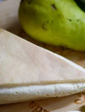 Stinking Bishop cheese, a glimpse of some celery, and a Bartlett pear on a cheeseboard.