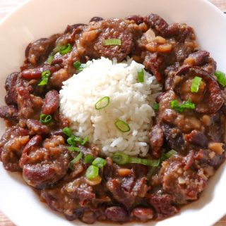 A white bowl containing rice surrounded by New Orleans style red beans, garnished with green onions.