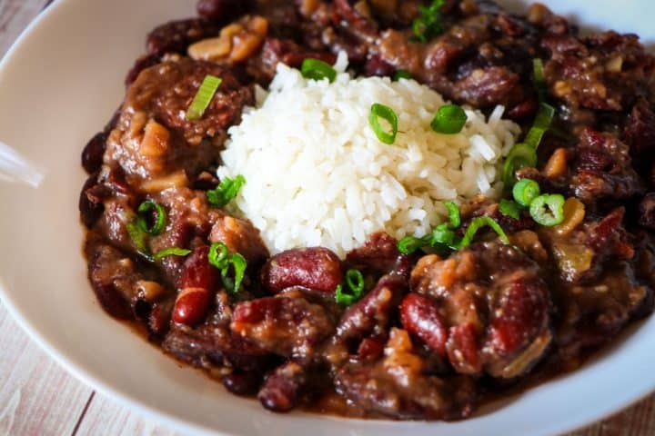 A white bowl containing rice surrounded by New Orleans style red beans, garnished with green onions.