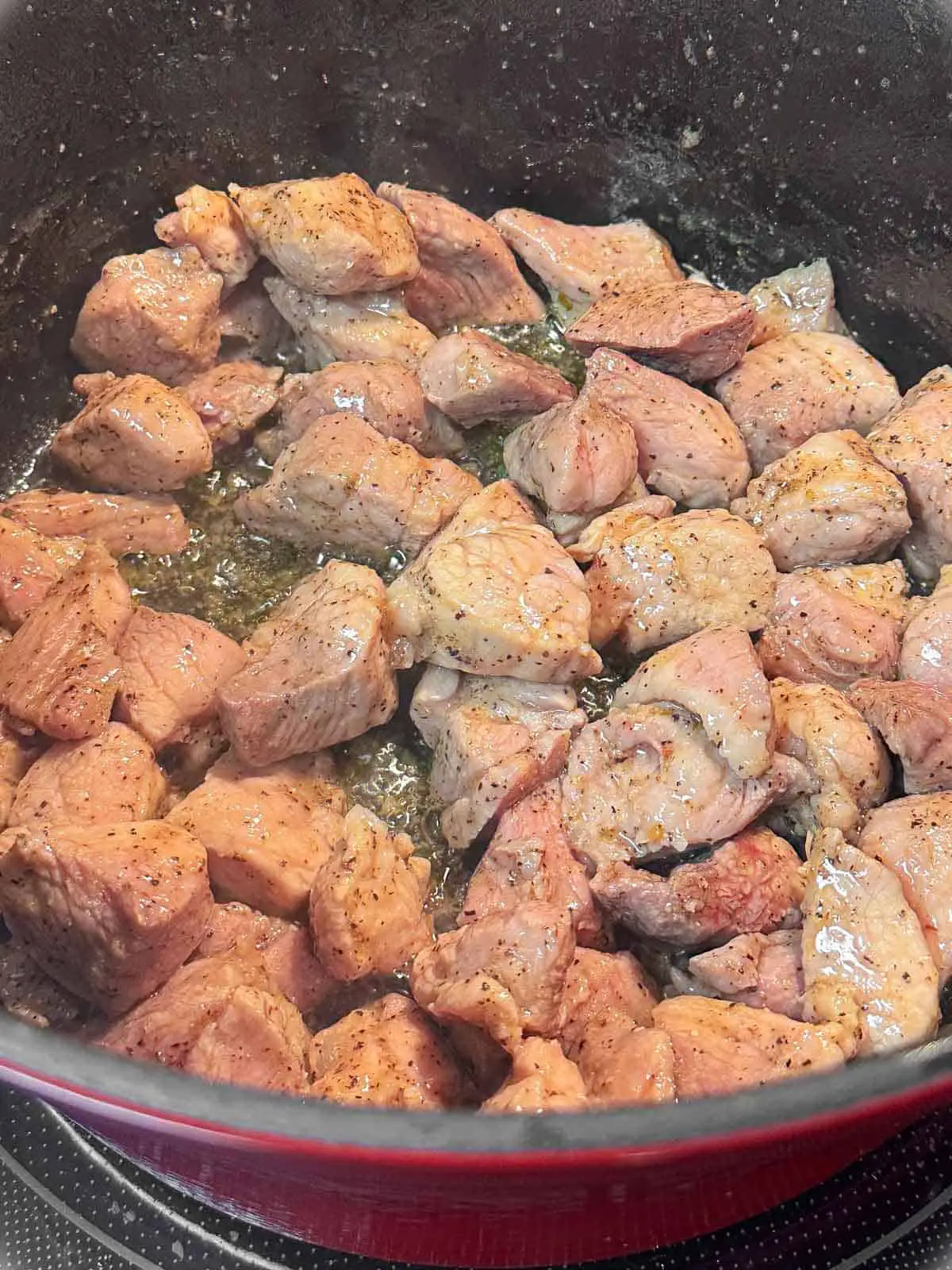 Pieces of pork shoulder browned in a large pot.