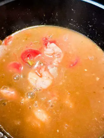 Gumbo broth with shrimp and stewed tomatoes in a large pot.