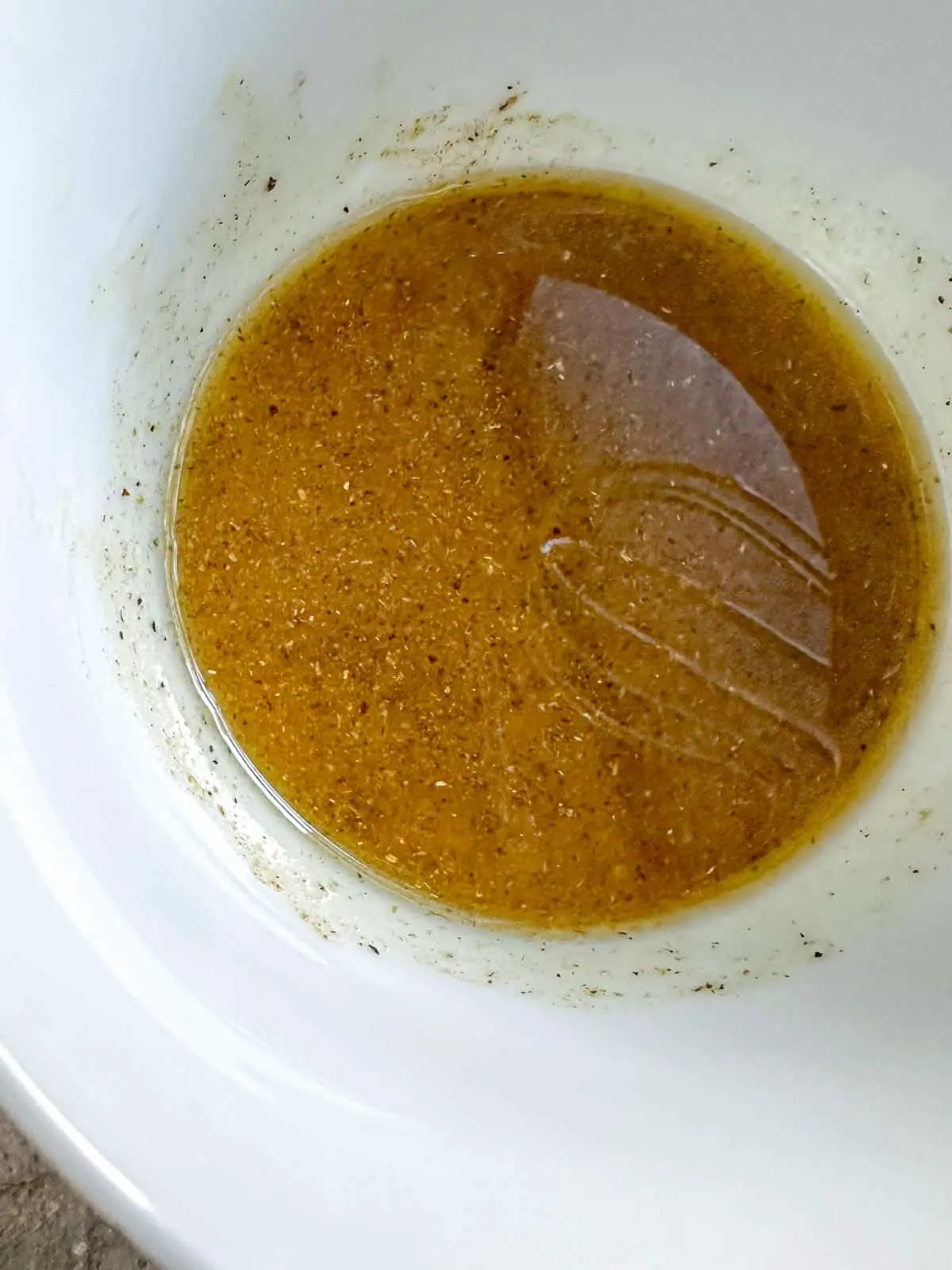 A white bowl containing a vinaigrette consisting of oil, vinegar, and seasonings.