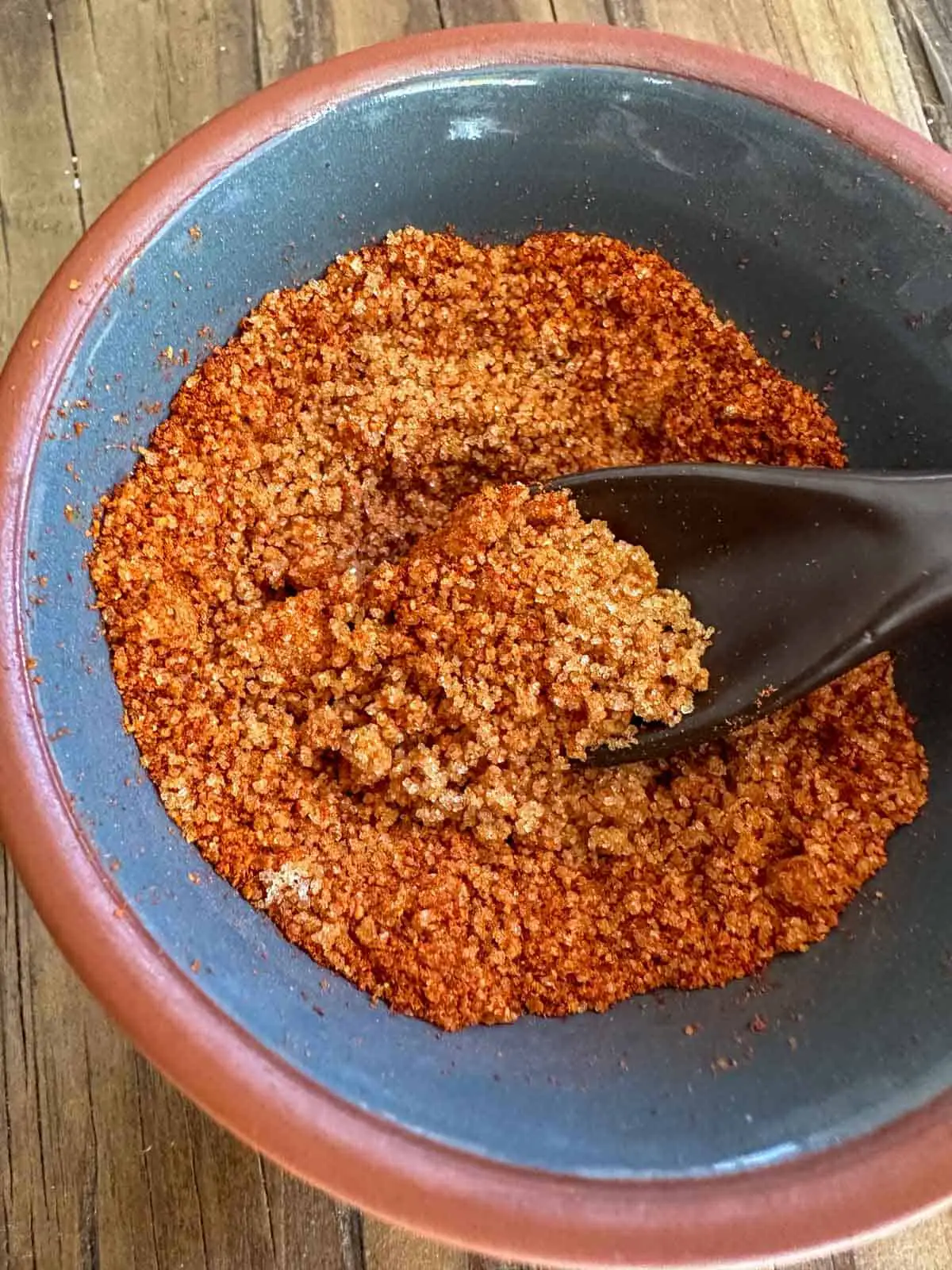 A small bowl containing a mixture of brown sugar and Scorpion pepper powder. There is a spoon with some of the mixture in it in the bowl.