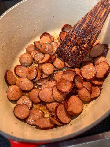 Sliced sausage in a large pot. There is a wooden utensil in the pot.