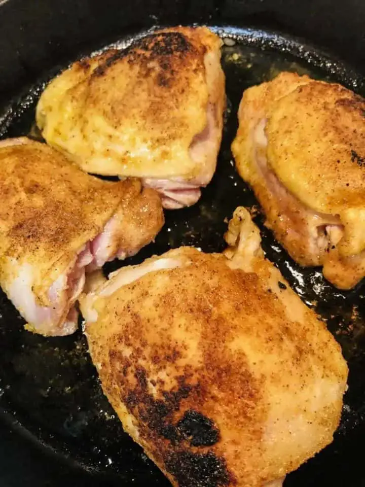 Browned bone in chicken thighs with skin in a cast iron pan.