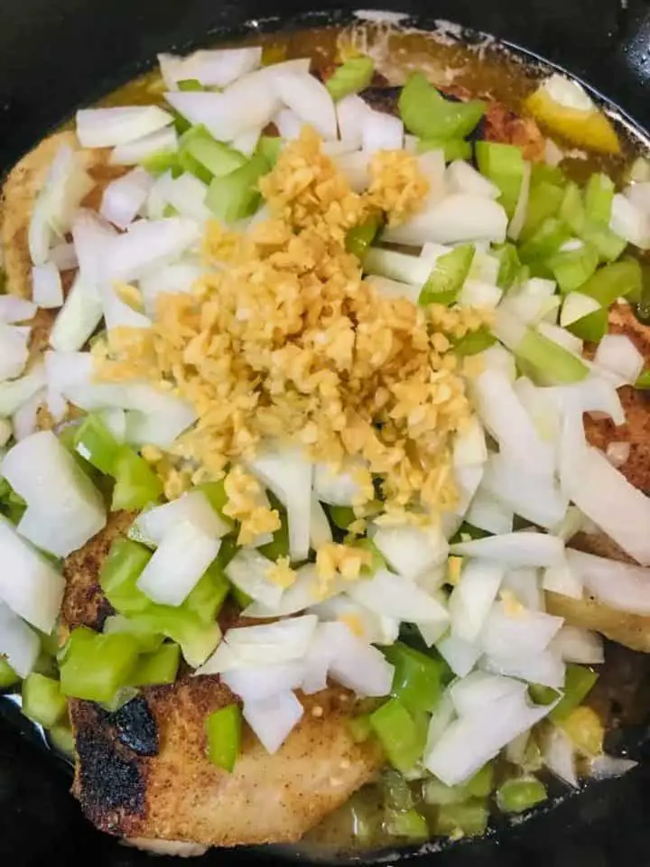 Browned chicken thighs covered with diced onion, minced garlic, diced celery and green bell pepper, and chicken broth.