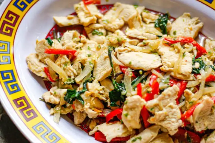 Slices of chicken along with onion, red bell pepper, and Thai basil on a patterned plate.