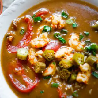 A white bowl containing shrimp gumbo with stewed tomatoes and sliced okra and green onions as garnish.