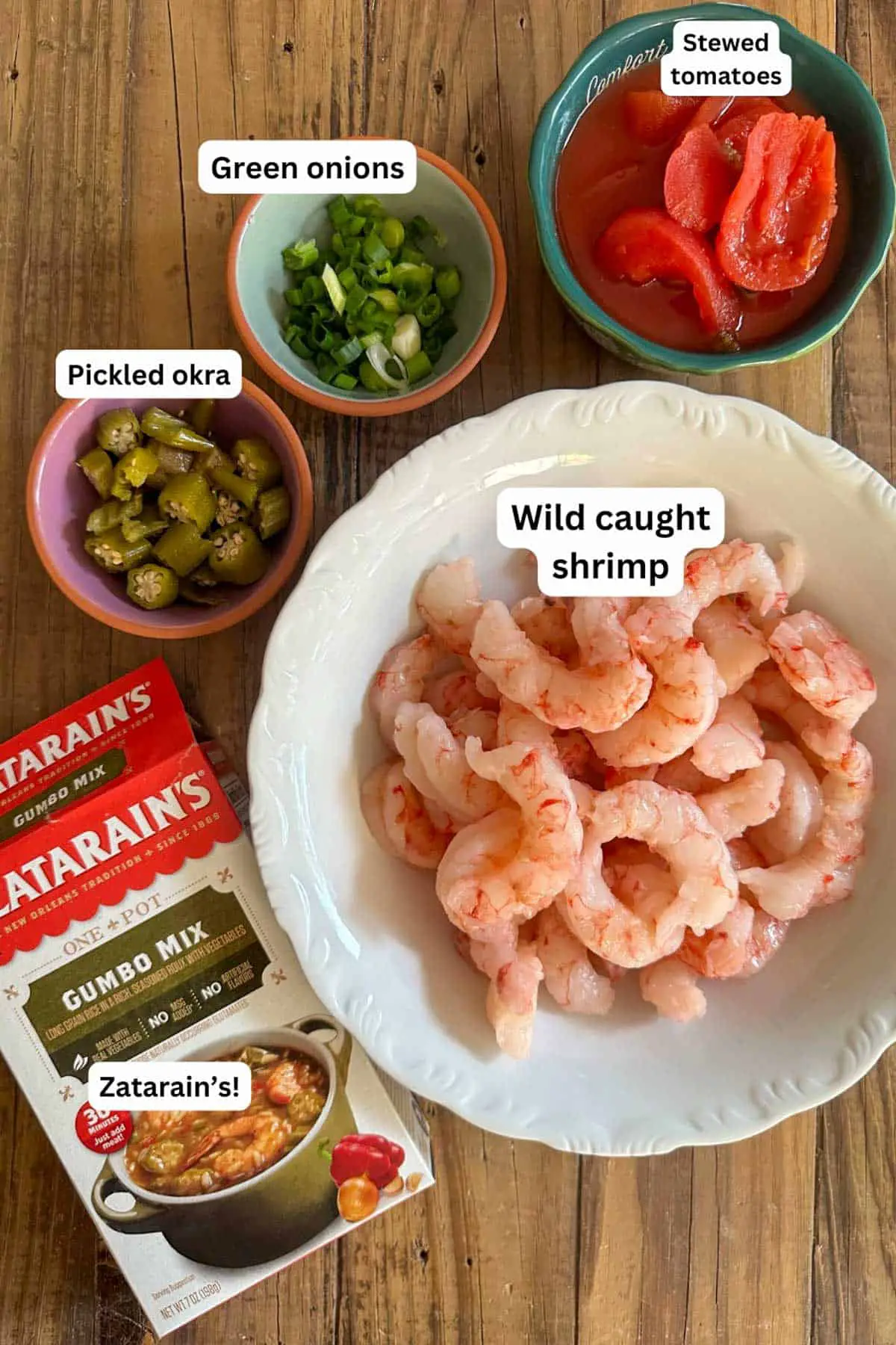 Ingredients for Zatarain's Shrimp Gumbo including a box of Zatarain's Gumbo Mix, and bowls containing wild caught shrimp, sliced pickled okra, sliced green onions, and stewed tomatoes.
