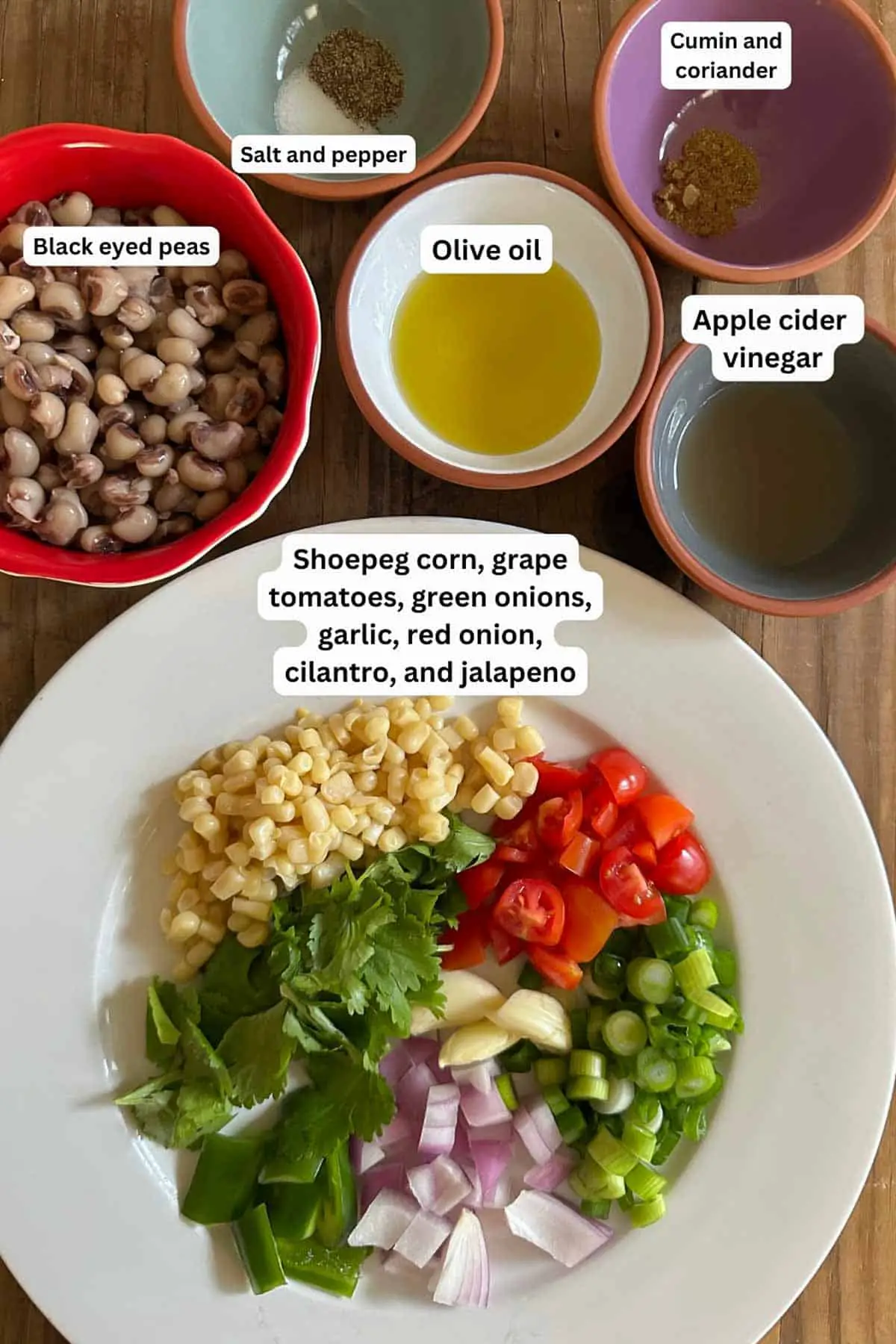 Ingredients of Texas caviar including black eyed peas, salt and pepper, cumin and coriander, olive oil, apple cider vinegar, shoepeg corn, grape tomatoes, green onions, garlic, red onion, cilantro, and jalapeno.