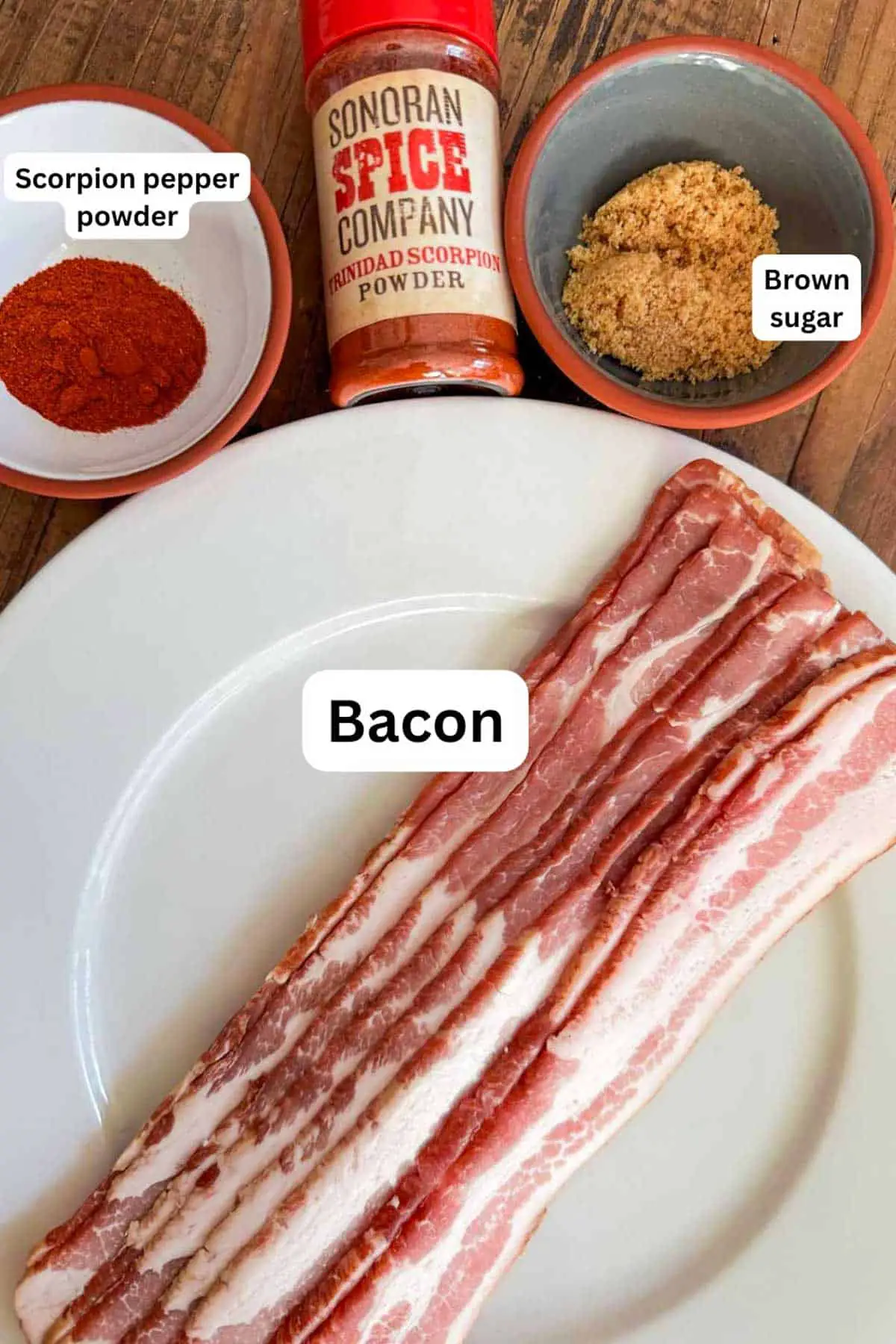 Bowls containing brown sugar and scorpion pepper powder, and uncooked bacon on a plate. There is also a bottle of Sonoran Spice Company Trinidad Scorpion Powder.