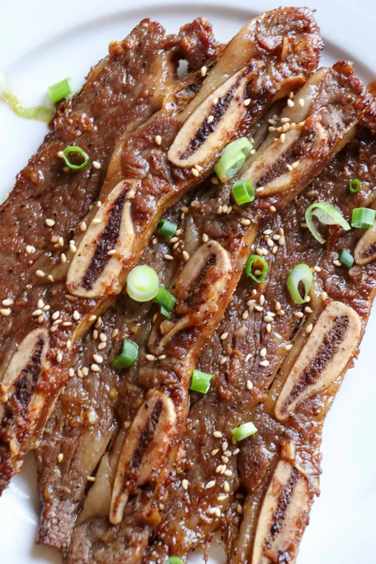 Korean Short Ribs garnished with sesame seeds and green onions on a white plate.