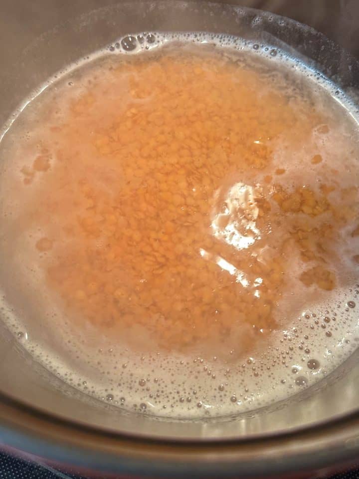 Red split lentils covered by water in a saucepan.