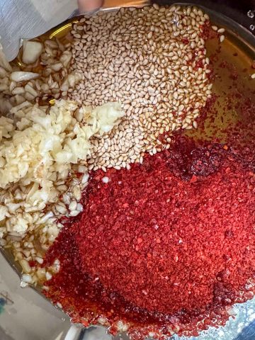 Sauce ingredients for Korean spicy bean sprouts in a large bowl including garlic, sesame seeds, sesame oil, fish sauce, and Korean red pepper flakes.