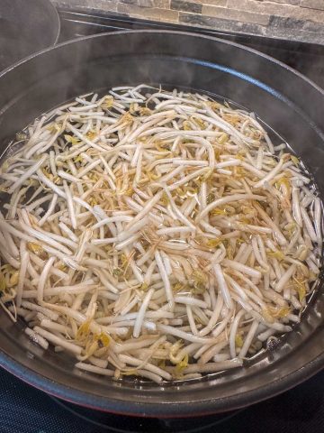Bean sprouts blanching in hot water in a large pot.