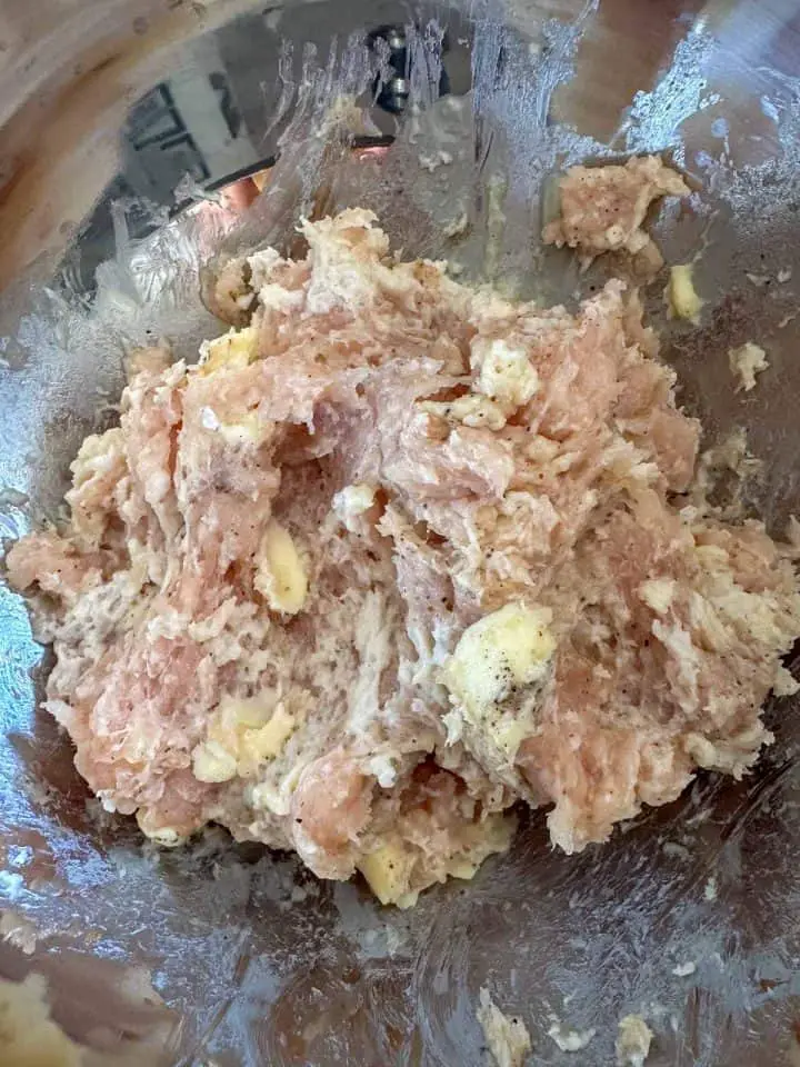 A mixture of ground chicken, seasonings, butter, and milk soaked bread in a mixing bowl.