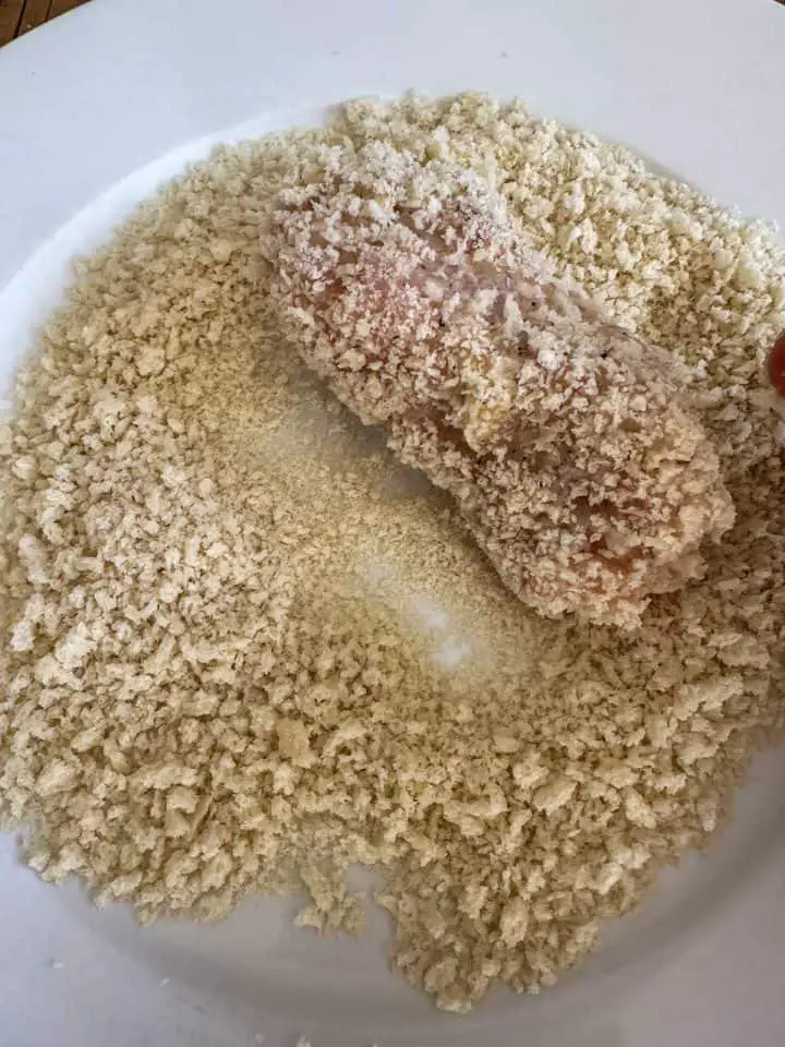 A ground chicken cutlet covered in panko on a panko covered plate.