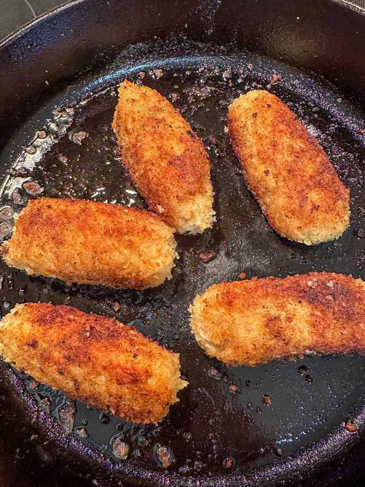 Golden brown ground chicken cutlets cooked in a cast iron skillet.
