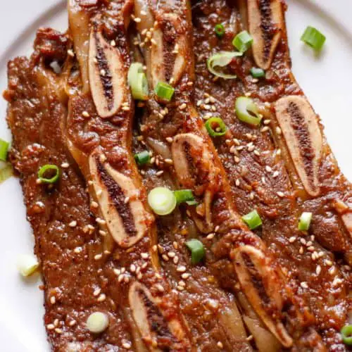 Korean Short Ribs garnished with sesame seeds and green onions on a white plate.