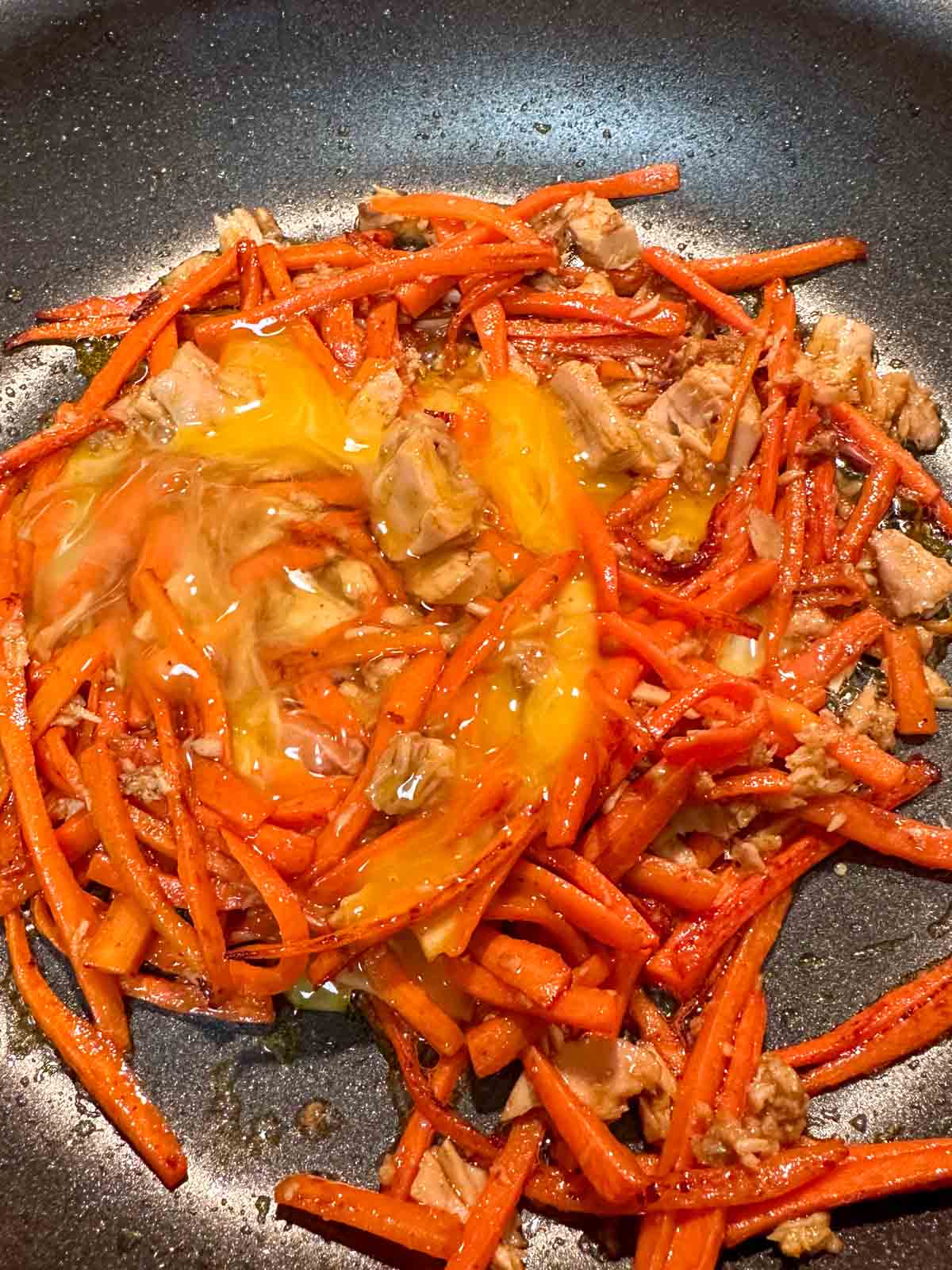 Julienned carrots cooked with tuna, seasonings, and whisked egg in a skillet.