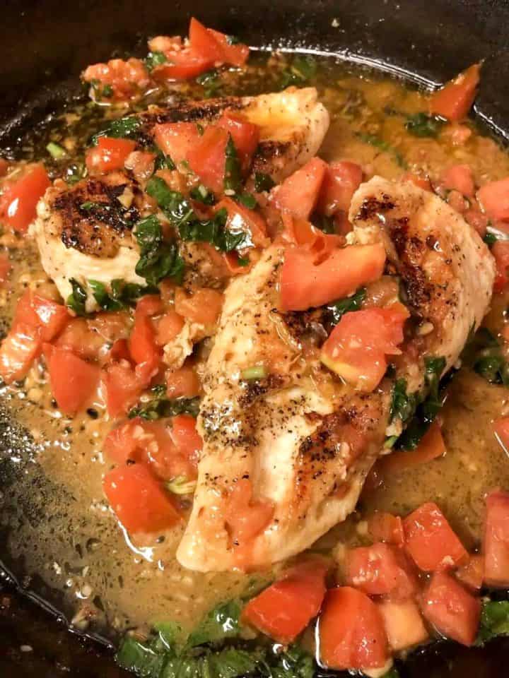 Tomato basil chicken which is hicken breasts with chopped tomatoes, garlic, and basil in a cast iron skillet.