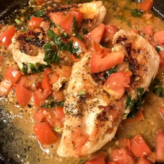 Tomato basil chicken which is hicken breasts with chopped tomatoes, garlic, and basil in a cast iron skillet.