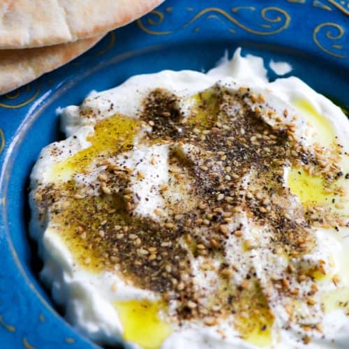 Labneh topped with olive oil and za'atar in a blue dish with pita bread.