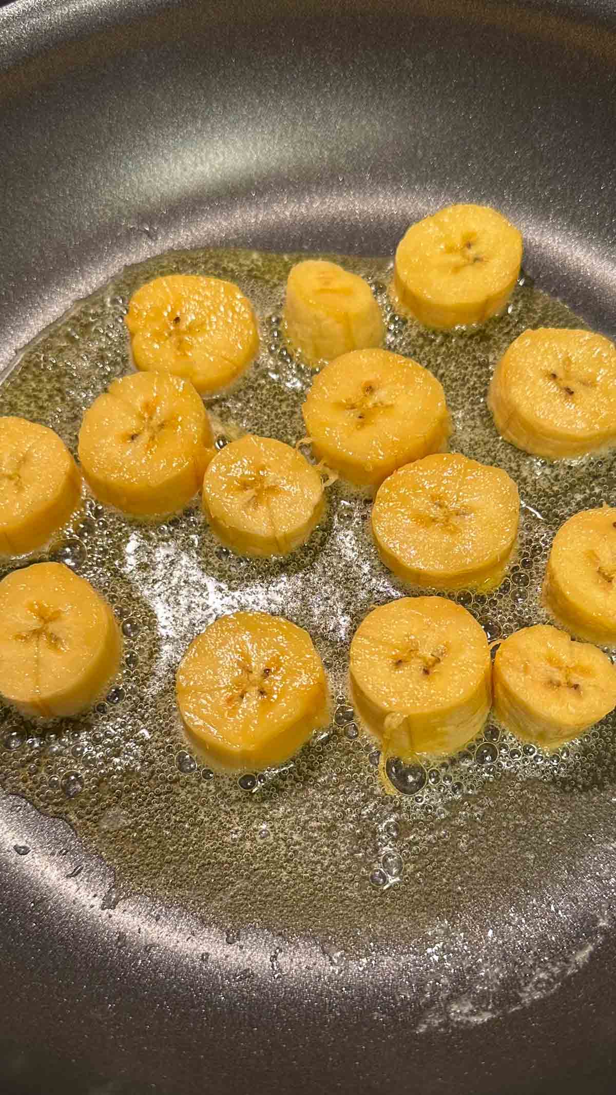 Sweet plantains that have been sliced frying in melted butter in a frying pan.