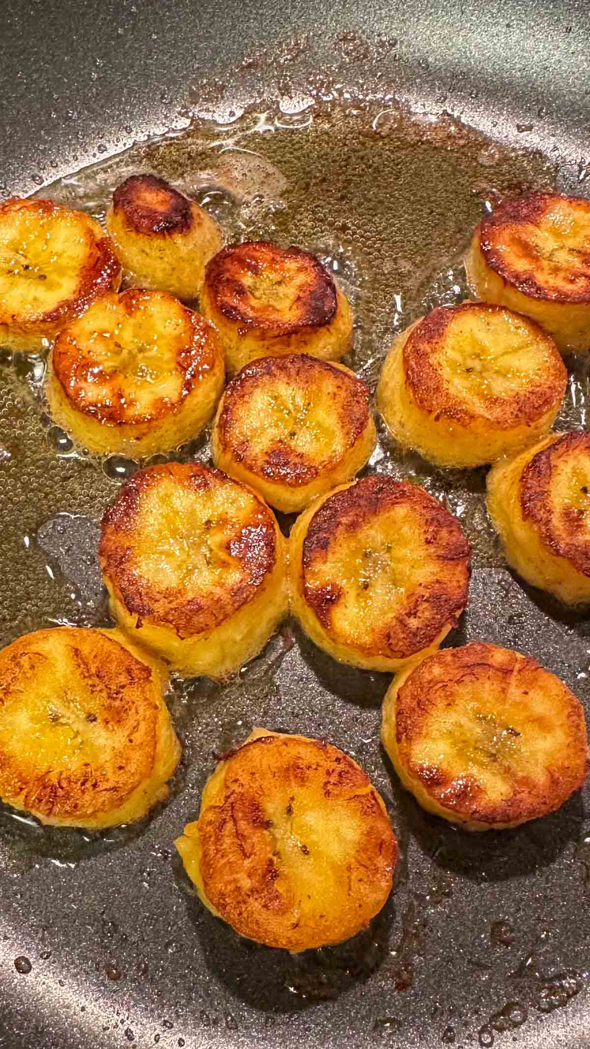 Sweet plantains that have been sliced and fried in butter. The plantains have been browned in the butter and are in a frying pan.