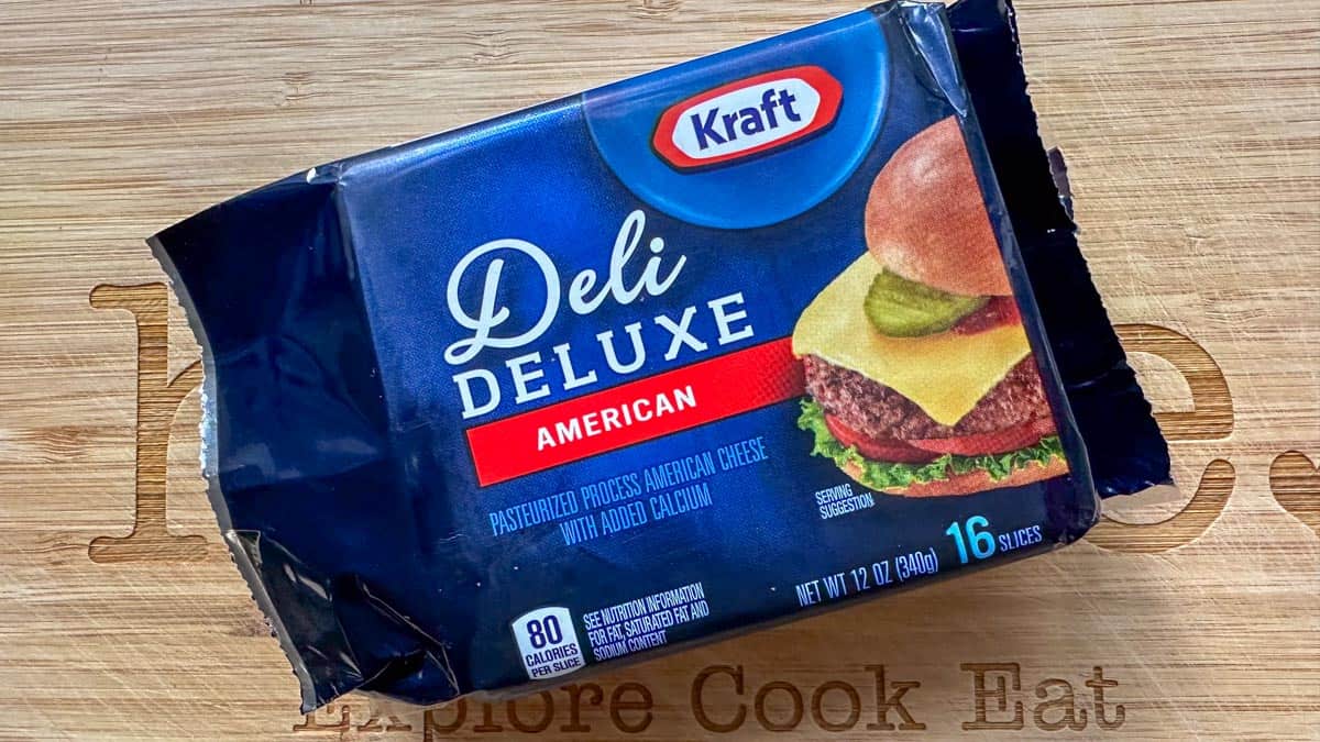 A package of Kraft American Deli Deluxe Cheese on a wooden cutting board.
