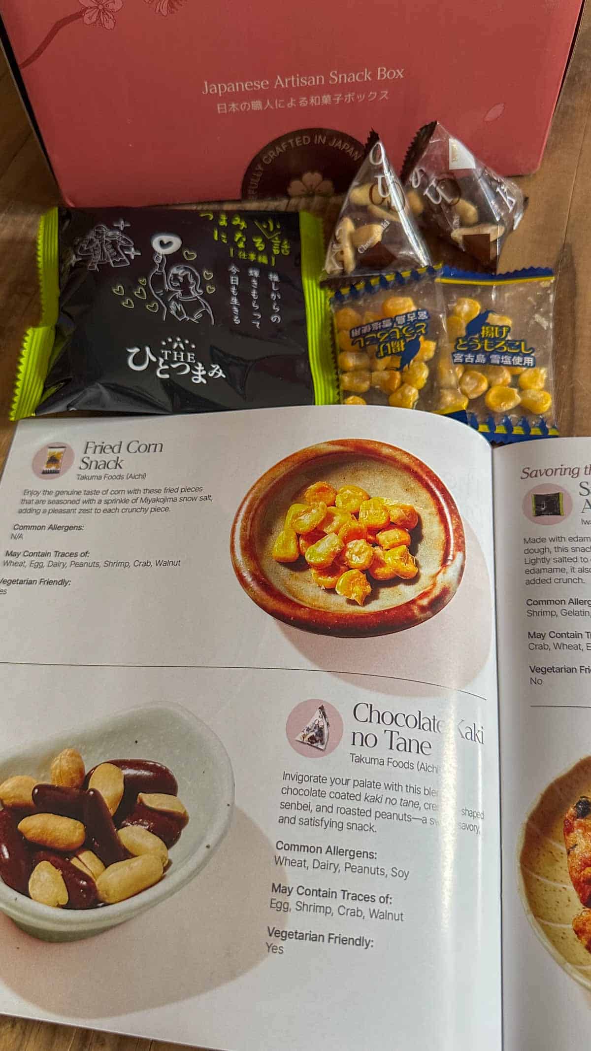 A selection of Japanese snacks and an opened Sakuraco Snack Guide displayed in front of a Sakuraco Japanese Artisan Snack Box.