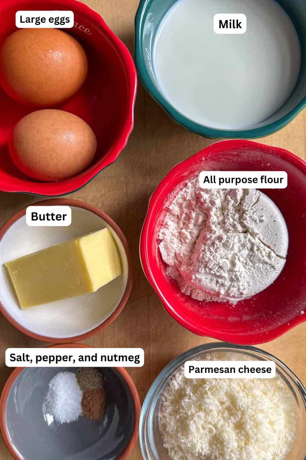 Ingredients needed to make Parmesan Cheese Drop Biscuits including large eggs, milk, butter, all purpose flour, Parmesan cheese, salt, pepper, and nutmeg all displayed in bowls.