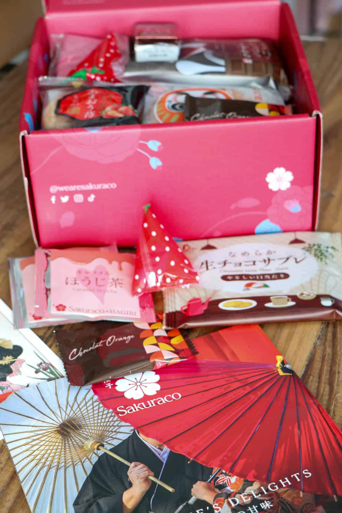 A Valentine themed Sakuraco box opened to show it full of Japanese snacks. The Snack Guide laid out in front of the box.