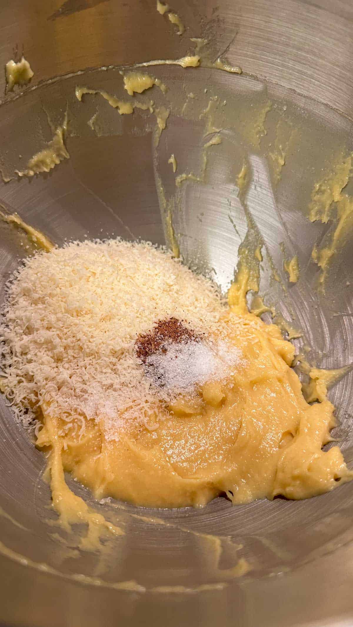 A dough mixture for Parmesan cheese drop biscuits topped with Parmesan cheese, salt, pepper, and nutmeg.