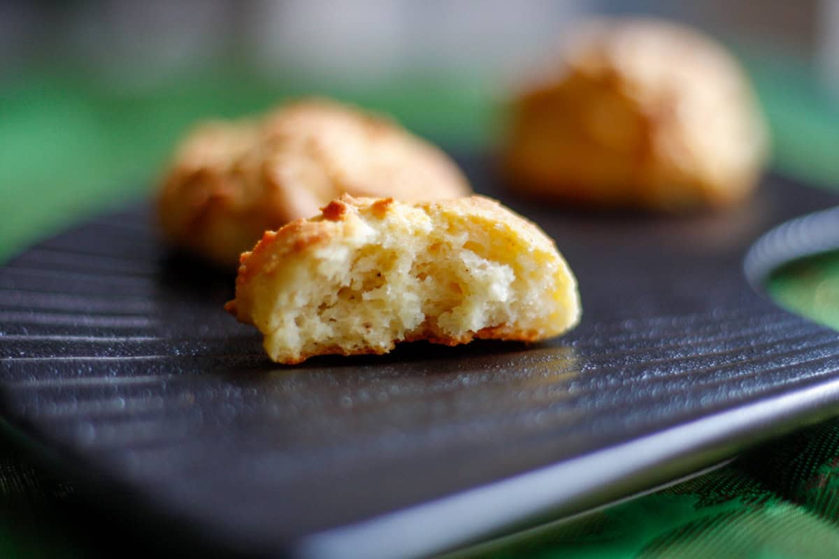 Parmesan cheese drop biscuits displayed on a black plate, with one cut in half to show the interior of the biscuit.