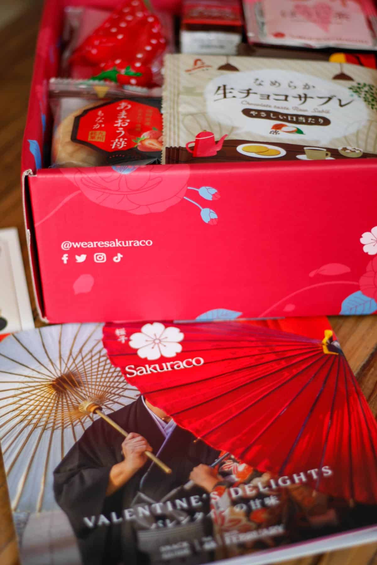 A Valentine themed Sakuraco box opened to show it full of Japanese snacks. The Snack Guide is laid out in front of the box.