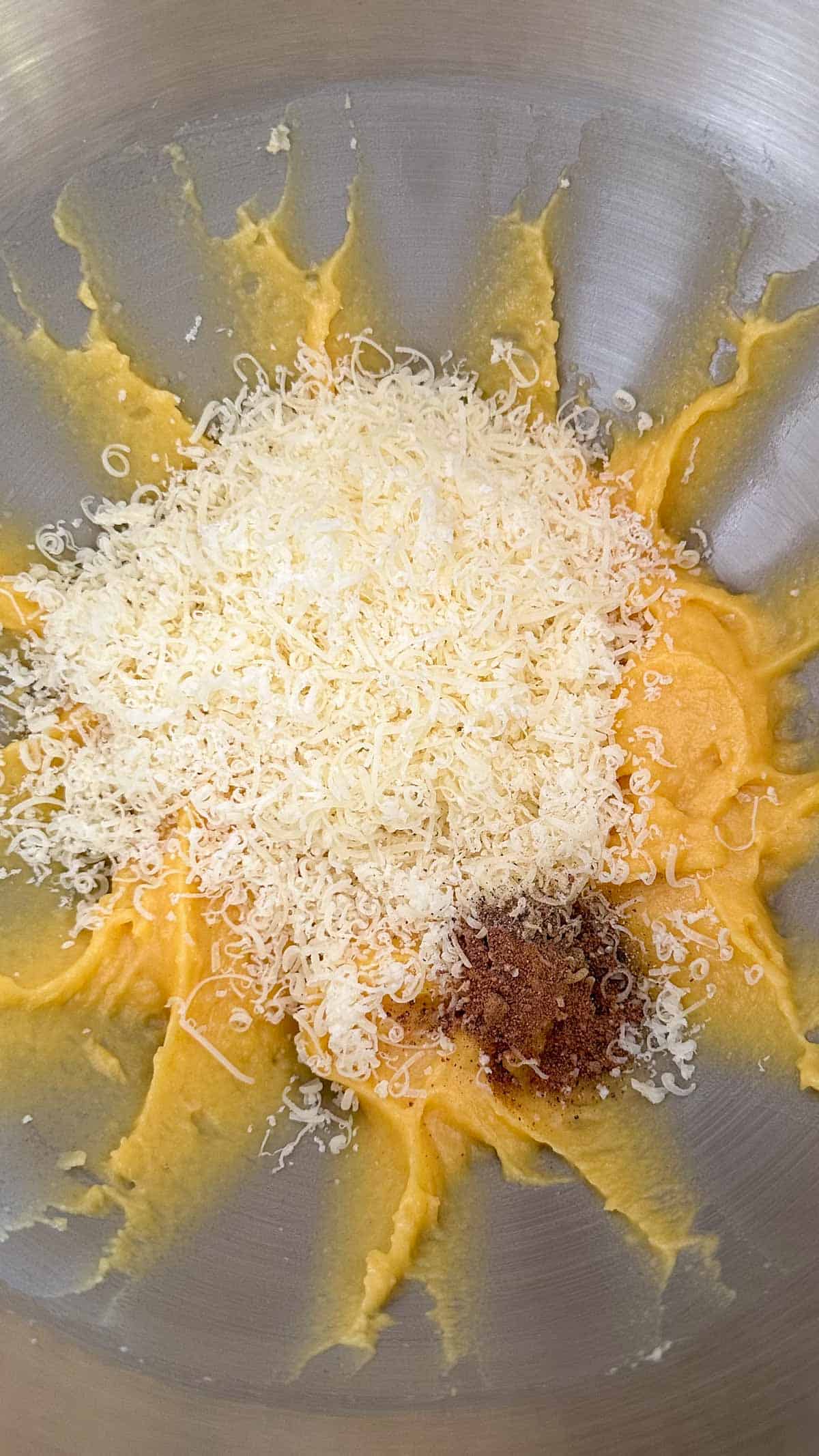 A stand mixer bowl containing Gruyere drop biscuit dough, seasonings, and finely grated Gruyere.