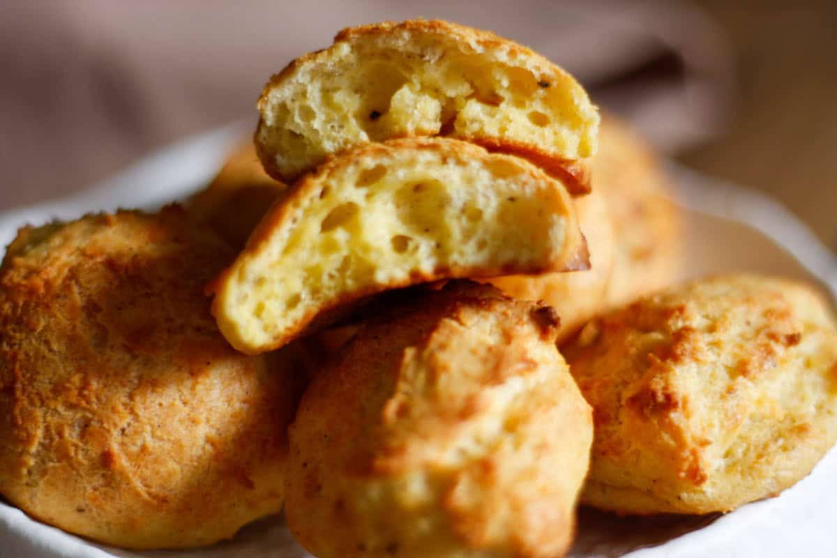 Gruyere drop biscuits on a serving plate. One of the biscuits has been cut in half to show the inside of the biscuit.