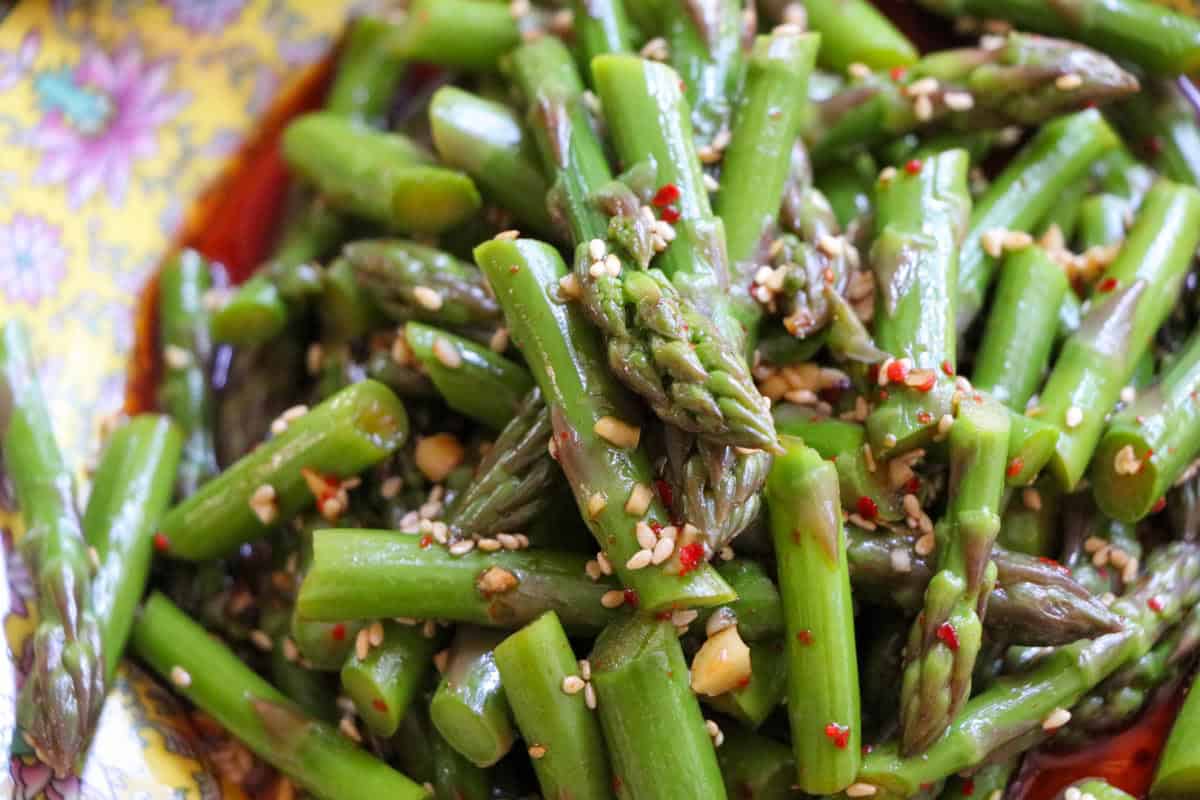 Asparagus with sesame seeds and sesame oil on a patterned plate.