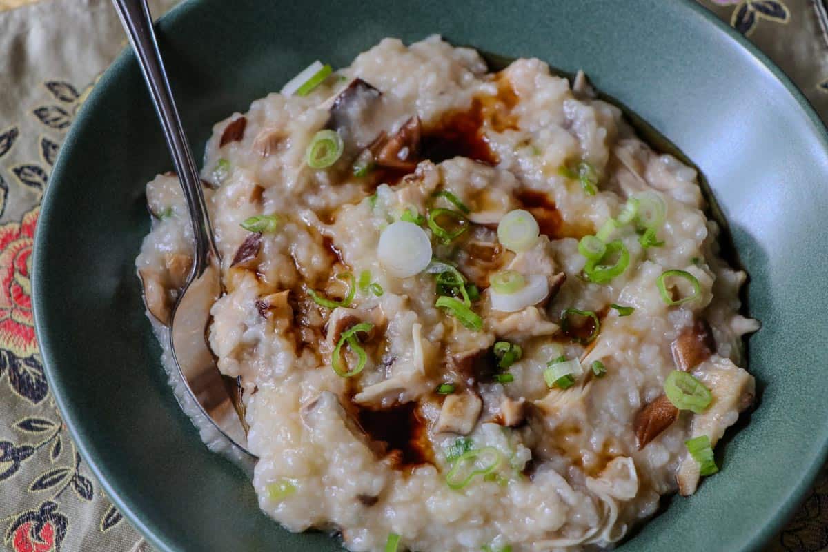 Korean style rice porridge (juk) with mushrooms, shredded chicken, and scallions in a green bowl with a spoon.