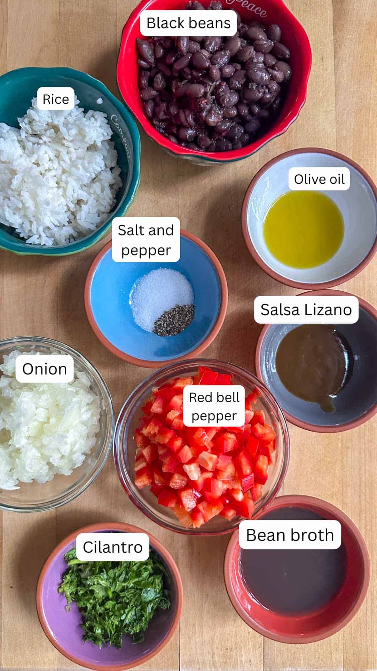 Gallo Pinto ingredients in bowls including black beans, rice, salt and pepper, olive oil, Salsa Lizano, onion, red bell pepper, cilantro, and bean broth.