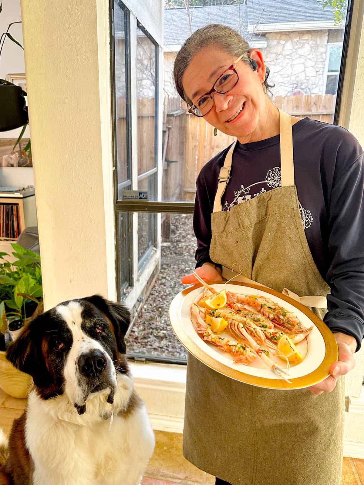 A woman holding a plate of New Zealand scampi next to a St. Bernard dog.