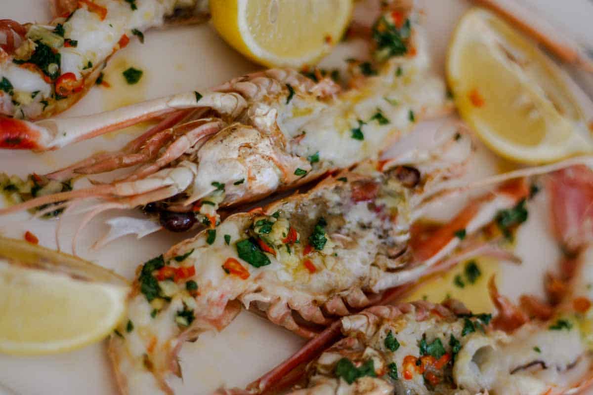 Broiled New Zealand scampi with garlic, chili, butter and parsley, served with lemon wedges.
