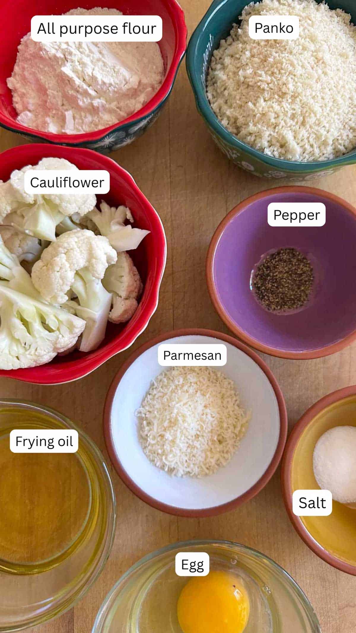 The ingredients to make Italian Style Fried Cauliflower displayed in bowls including flour, panko, cauliflower, pepper, Parmesan, frying oil, salt, and egg.