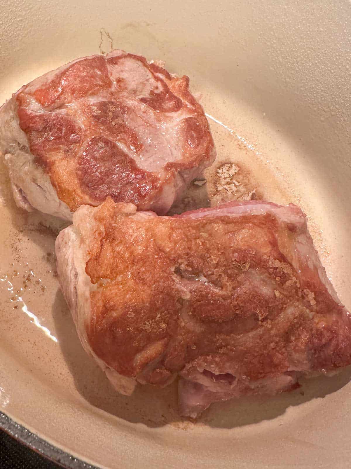 A red Dutch oven containing pieces of browned pork butt.