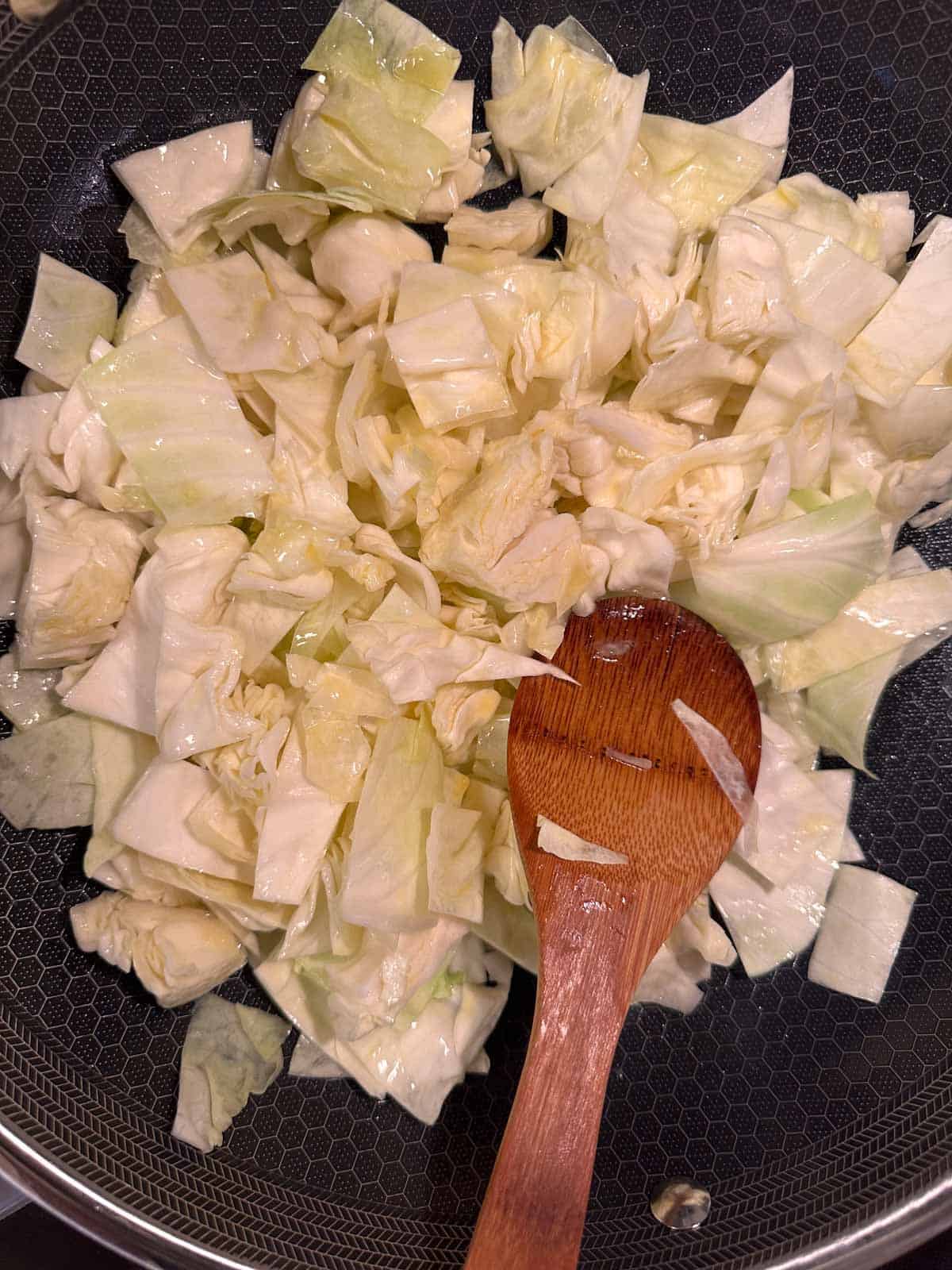 Chopped cabbage in a wok with a wooden spoon.