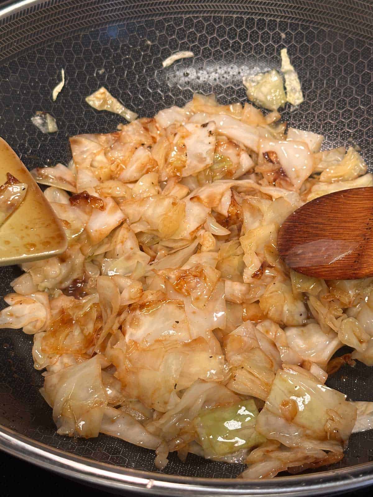 Caramelized sautéed cabbage in a wok with a spatula and wooden spoon.
